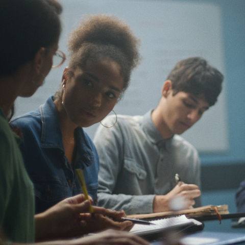 Três estudantes conversam e fazem anotações em seus cadernos